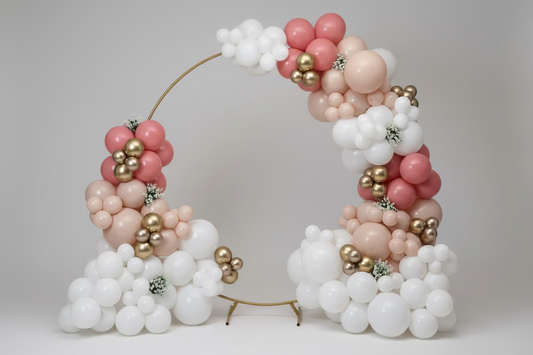 Balloon arch with pink, white, and gold balloons against a plain wall.