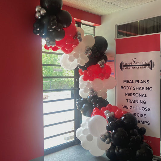 Balloon arch with red, black, and white balloons in front of a gym sign.